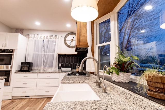 kitchen featuring sink, light hardwood / wood-style flooring, double oven, light stone counters, and white cabinetry