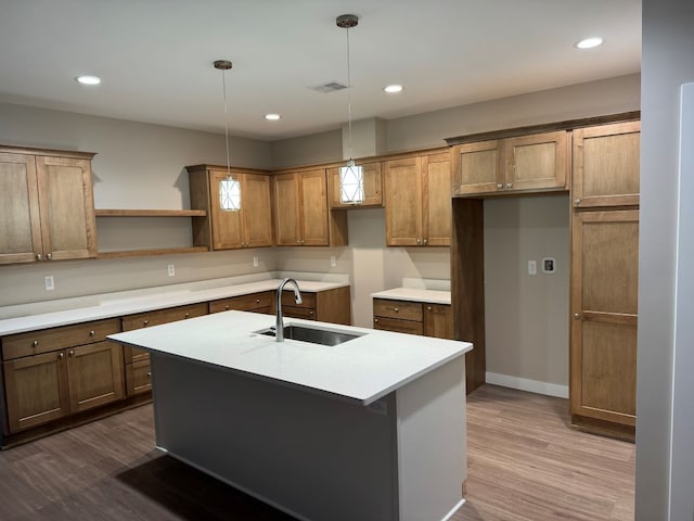 kitchen with sink, decorative light fixtures, hardwood / wood-style floors, and an island with sink