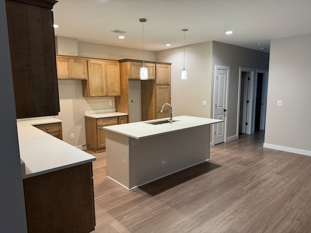 kitchen with sink, dark hardwood / wood-style flooring, a kitchen island with sink, and pendant lighting