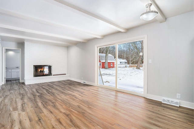 unfurnished living room featuring a fireplace, beamed ceiling, and wood-type flooring