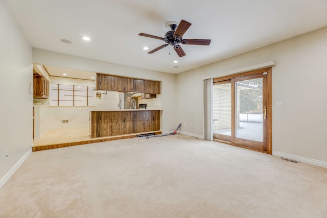 unfurnished living room with ceiling fan, light colored carpet, and sink