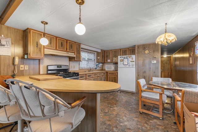 kitchen featuring white appliances, an inviting chandelier, hanging light fixtures, wood walls, and kitchen peninsula