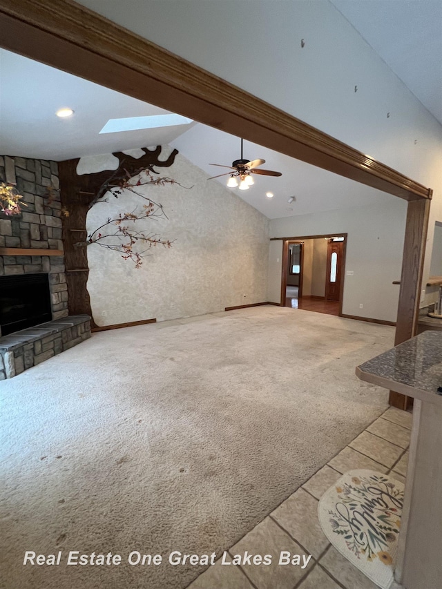 unfurnished living room featuring carpet flooring, lofted ceiling with skylight, a fireplace, and ceiling fan