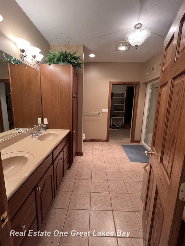 bathroom featuring tile patterned flooring, vanity, a shower with shower door, and toilet