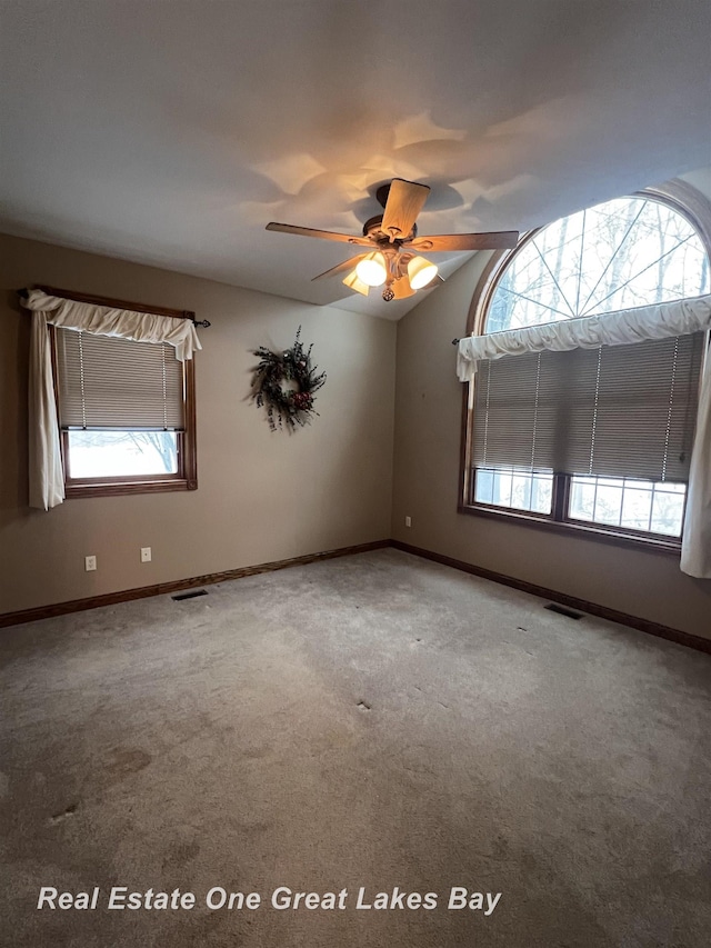 carpeted empty room featuring ceiling fan, a wealth of natural light, and vaulted ceiling