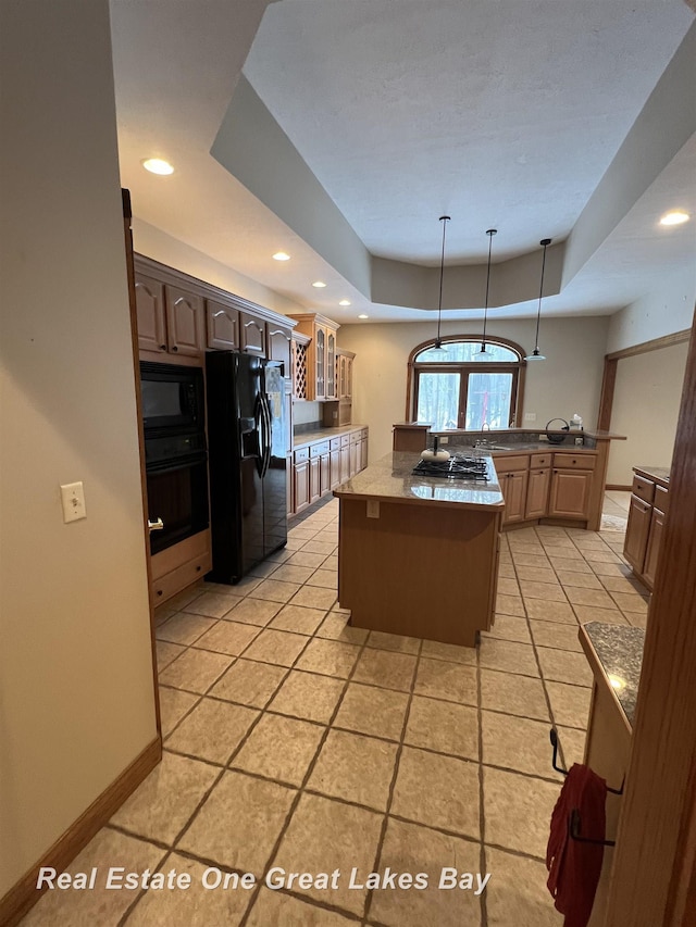 kitchen featuring pendant lighting, a center island, black appliances, a raised ceiling, and light tile patterned floors