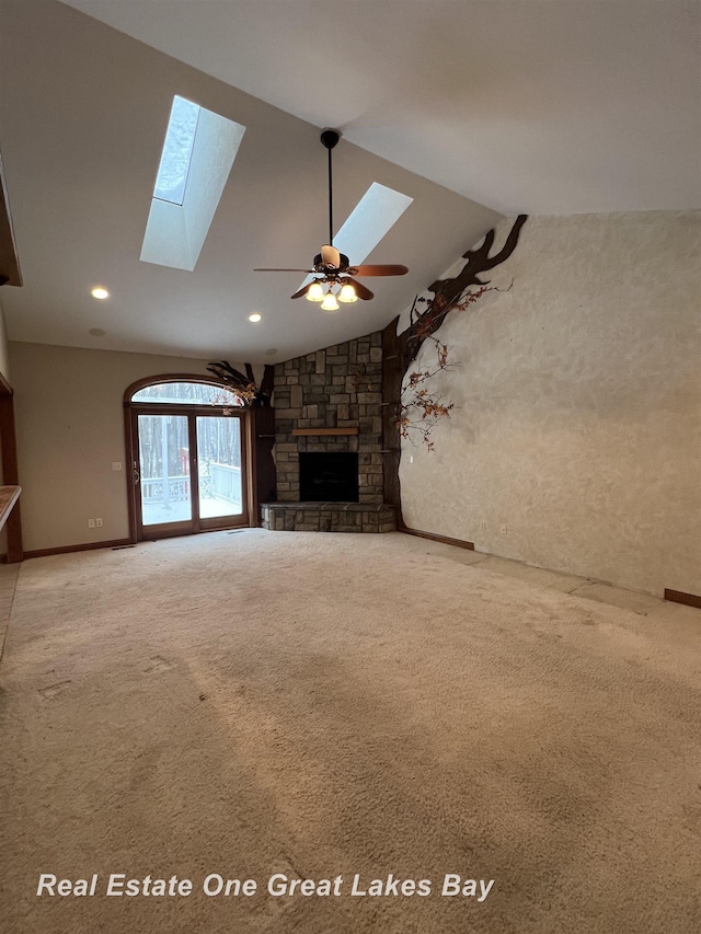 unfurnished living room featuring a fireplace, carpet, lofted ceiling with skylight, and ceiling fan