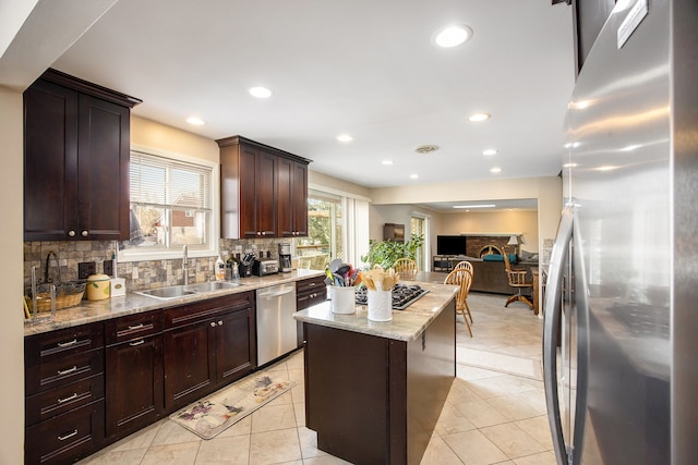 kitchen featuring sink, backsplash, stainless steel appliances, a center island, and light stone counters