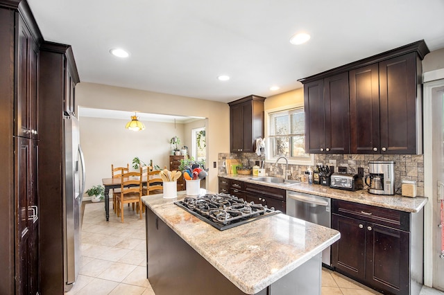 kitchen with sink, stainless steel appliances, light stone countertops, a kitchen island, and decorative light fixtures