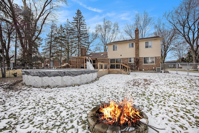 snow covered back of property with cooling unit, a swimming pool side deck, and an outdoor fire pit