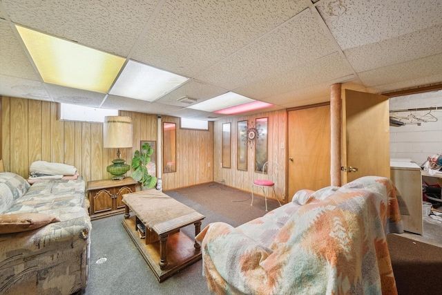 living room featuring dark colored carpet, wooden walls, and a drop ceiling