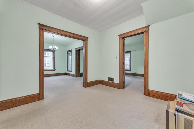 spare room featuring plenty of natural light, light colored carpet, and a notable chandelier