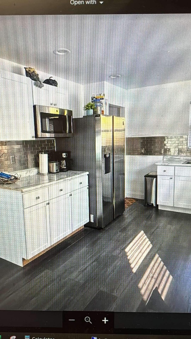 kitchen with appliances with stainless steel finishes, white cabinets, light stone countertops, and decorative backsplash