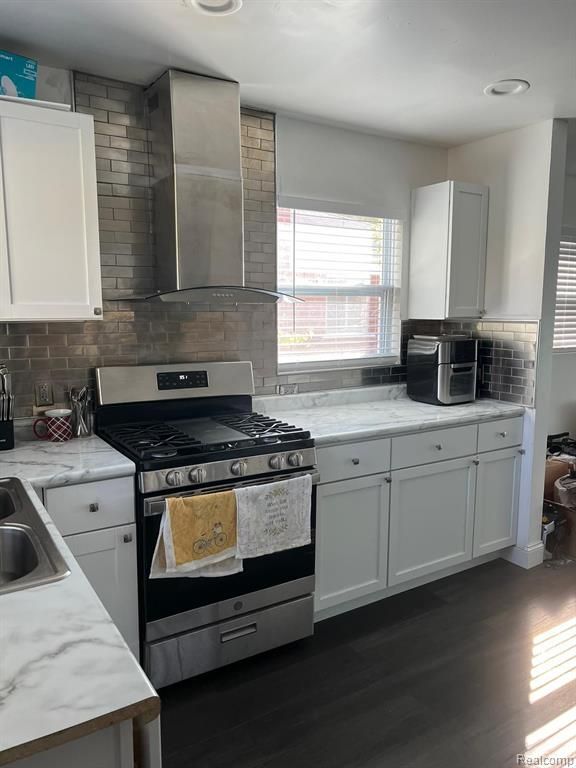 kitchen with gas range, wall chimney exhaust hood, and white cabinetry