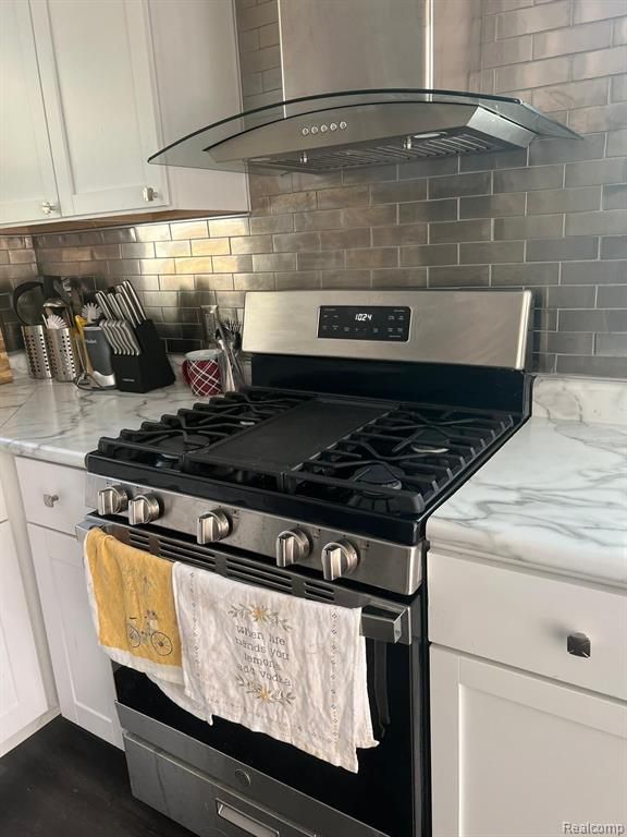 kitchen featuring gas stove, white cabinets, backsplash, and light stone countertops