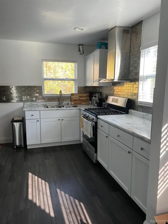 kitchen featuring dark wood-style flooring, gas stove, white cabinets, a sink, and wall chimney range hood