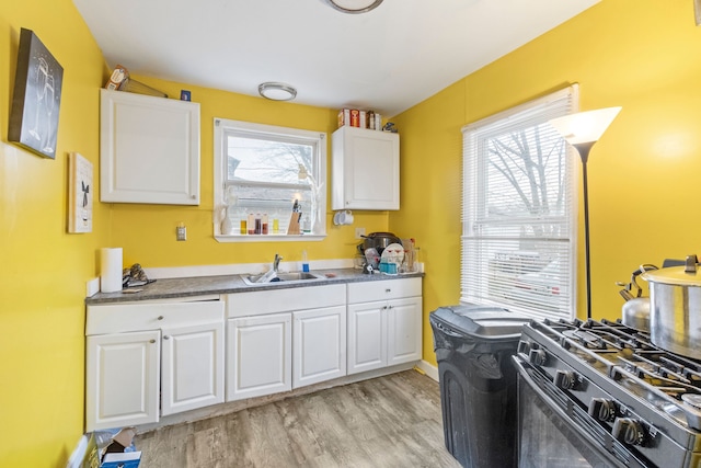 kitchen with gas stove, white cabinetry, sink, a healthy amount of sunlight, and light wood-type flooring