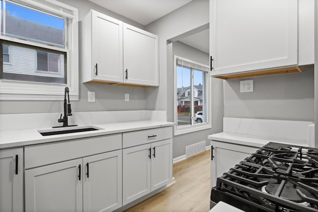 kitchen with black range with gas stovetop, sink, white cabinets, and light wood-type flooring