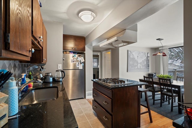 kitchen featuring exhaust hood, a kitchen bar, appliances with stainless steel finishes, dark brown cabinets, and sink