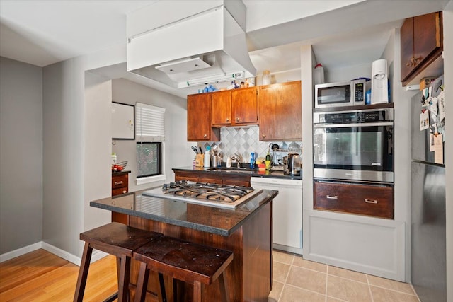 kitchen featuring tasteful backsplash, sink, island exhaust hood, a breakfast bar area, and stainless steel appliances