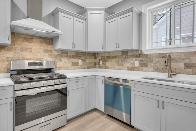 kitchen featuring sink, wall chimney exhaust hood, light wood-type flooring, tasteful backsplash, and appliances with stainless steel finishes