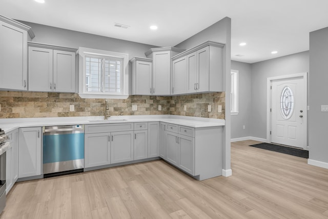 kitchen featuring sink, light hardwood / wood-style flooring, decorative backsplash, gray cabinets, and appliances with stainless steel finishes