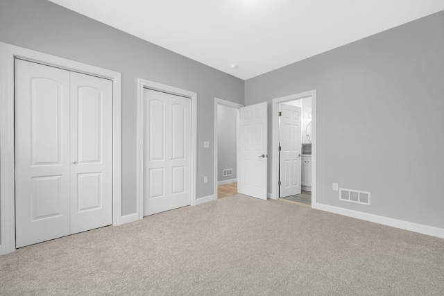 unfurnished bedroom featuring two closets, connected bathroom, and light colored carpet