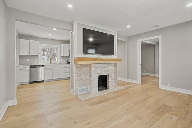 unfurnished living room featuring light hardwood / wood-style flooring, a stone fireplace, and sink