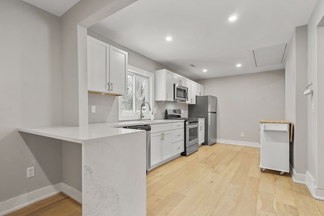 kitchen with white cabinetry, kitchen peninsula, stainless steel appliances, light hardwood / wood-style flooring, and sink