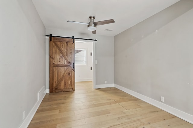 spare room featuring ceiling fan, light hardwood / wood-style flooring, and a barn door