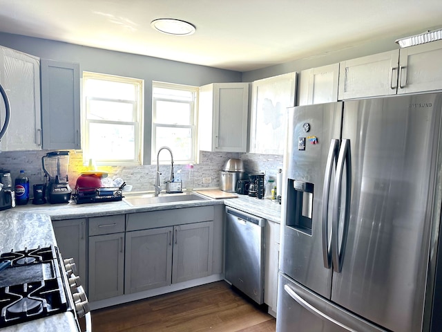 kitchen with decorative backsplash, appliances with stainless steel finishes, dark wood-type flooring, sink, and gray cabinets