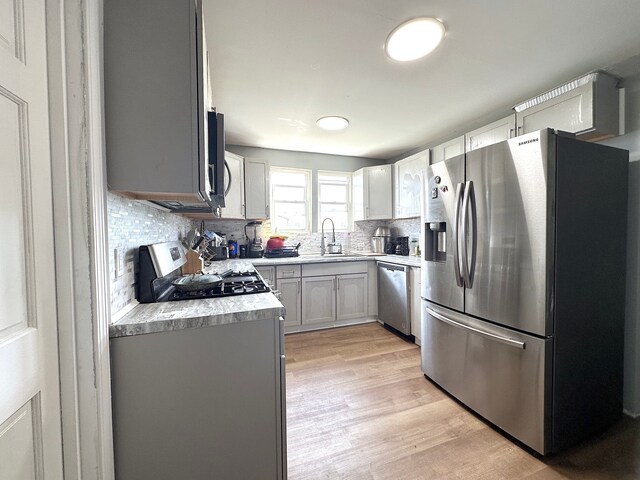 kitchen featuring light wood-type flooring, sink, appliances with stainless steel finishes, and tasteful backsplash