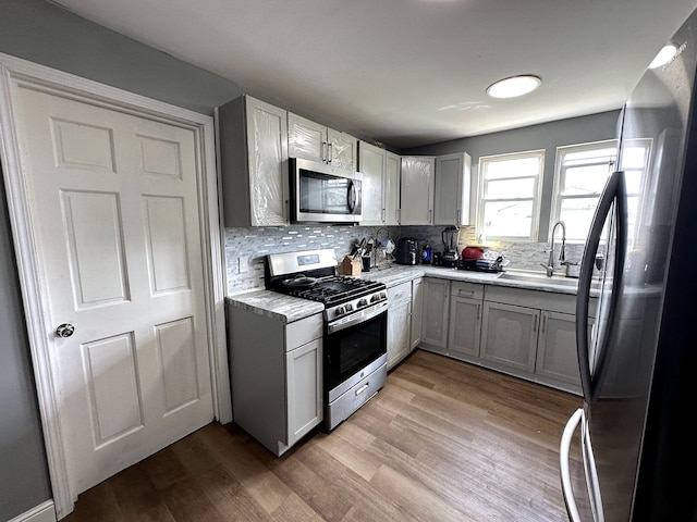 kitchen featuring gray cabinetry, backsplash, sink, light wood-type flooring, and appliances with stainless steel finishes