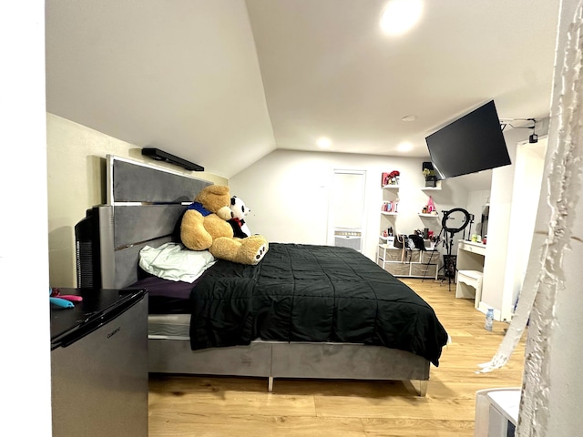 bedroom with light wood-type flooring, fridge, and lofted ceiling