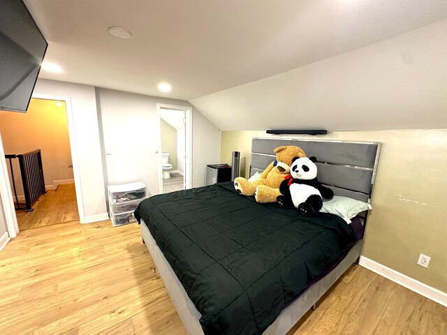 bedroom with vaulted ceiling, connected bathroom, and light hardwood / wood-style flooring