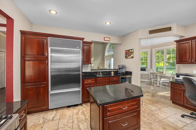 kitchen with dark stone countertops, built in fridge, sink, and a center island