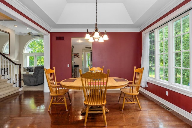 dining space featuring dark hardwood / wood-style floors, vaulted ceiling, ceiling fan with notable chandelier, and a tray ceiling