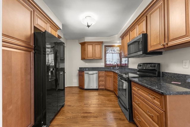 kitchen with appliances with stainless steel finishes, dark wood-type flooring, dark stone counters, and sink