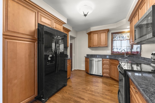 kitchen featuring appliances with stainless steel finishes, hardwood / wood-style floors, dark stone countertops, and sink