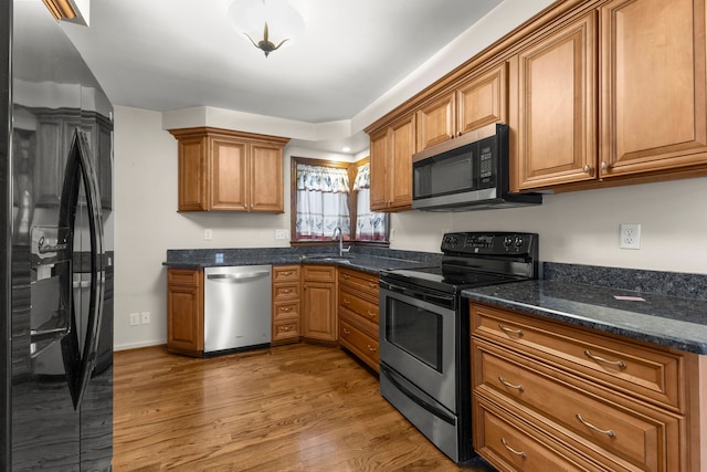 kitchen with stainless steel appliances, dark stone countertops, hardwood / wood-style flooring, and sink