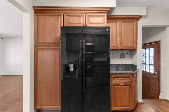 kitchen featuring black fridge, light wood-type flooring, and dark stone counters