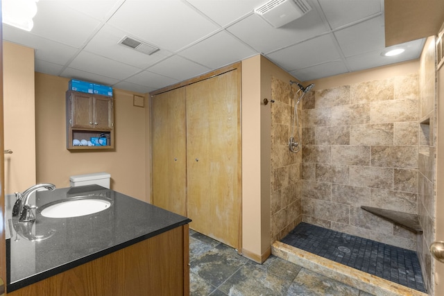 bathroom with toilet, a drop ceiling, a tile shower, and vanity