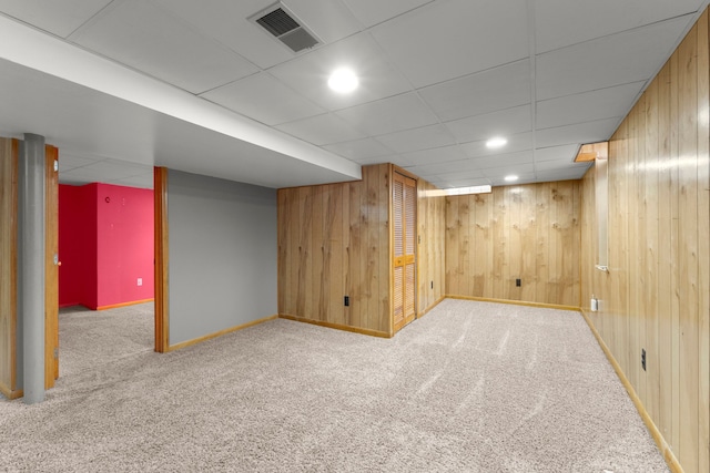 basement with wooden walls, a paneled ceiling, and carpet