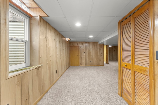 basement with light colored carpet, a paneled ceiling, and wooden walls