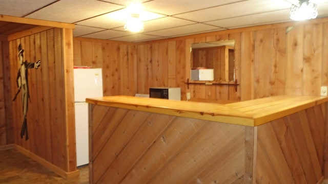 bar with a paneled ceiling, white fridge, and wood walls