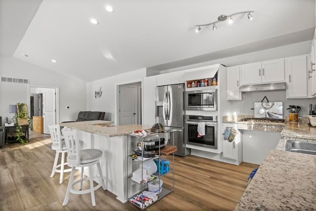 kitchen with light stone counters, white cabinetry, stainless steel appliances, and vaulted ceiling