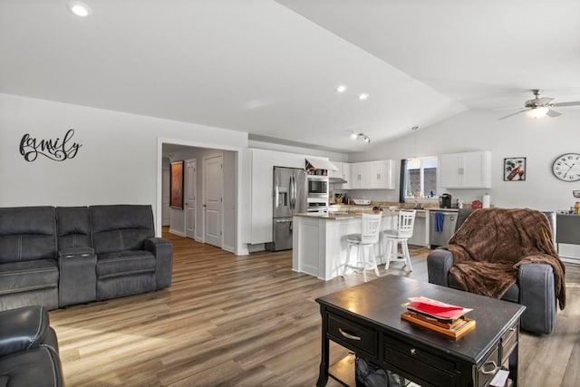 living room featuring ceiling fan, light hardwood / wood-style flooring, and vaulted ceiling