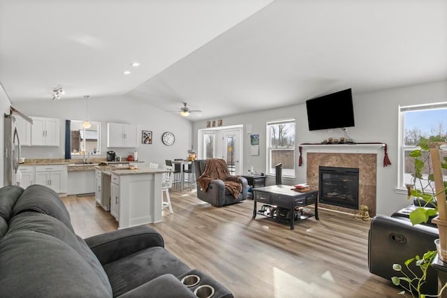 living room with ceiling fan, vaulted ceiling, a premium fireplace, and light hardwood / wood-style flooring