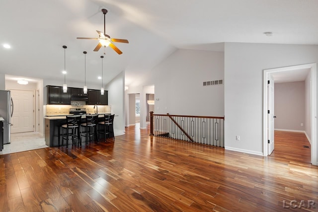 living room with dark hardwood / wood-style floors, ceiling fan, sink, and high vaulted ceiling