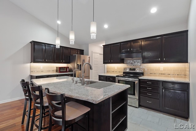 kitchen with a kitchen breakfast bar, hanging light fixtures, an island with sink, light stone counters, and stainless steel appliances